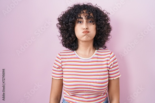 Young middle east woman standing over pink background puffing cheeks with funny face. mouth inflated with air, crazy expression. © Krakenimages.com