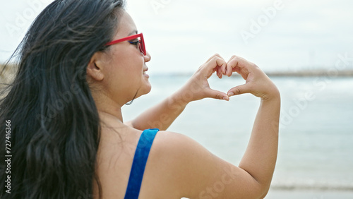 Young chinese woman tourist wearing bikini doing heart gesture at the beach