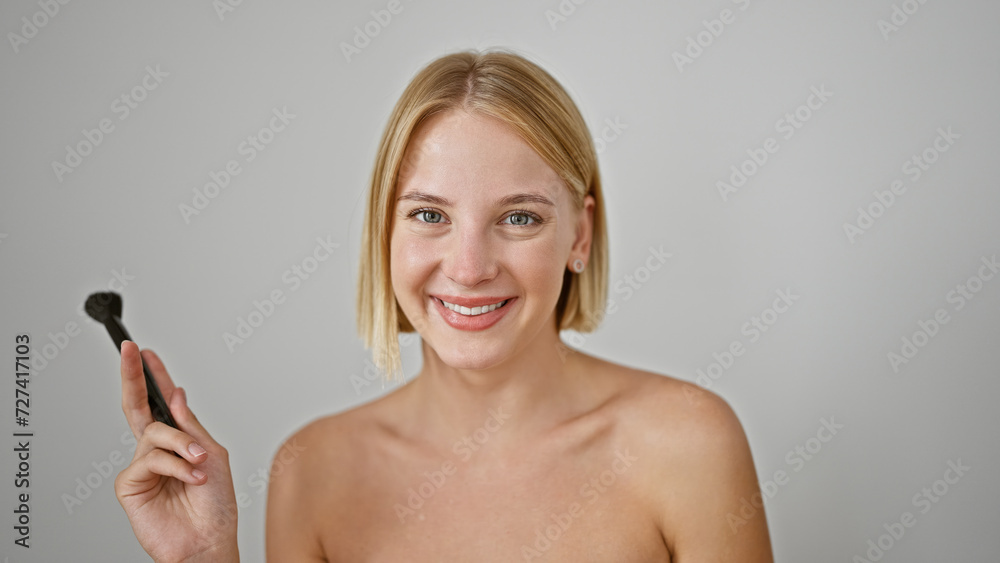 Young blonde woman smiling confident holding make up brush over isolated white background Young blonde woman smiling confident holding make up brush over isolated white background