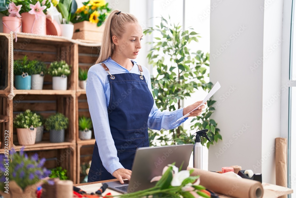 Young blonde woman florist using laptop reading document at florist