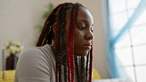 Beautiful african american woman sitting on living room sofa, sporting braids and a serious worry-laden expression, sparking ideas of doubt, sadness, indoors at her comforting apartment home