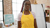 Commanding presence, beautiful, relaxed african american woman artist, donning braids and apron, masterfully standing amid the fervor of art school studio, engrossed in the joyful process of painting