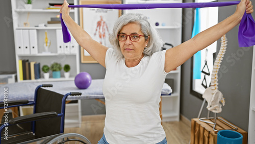 Mature woman exercising with resistance band in rehab clinic alongside wheelchair photo