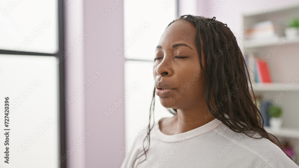A serene young african american woman with curly hair meditating in a bright modern living room. A serene young african american woman with curly hair meditating in a bright modern living room.