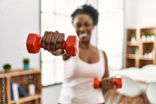 African american woman smiling confident using dumbbells boxing at home