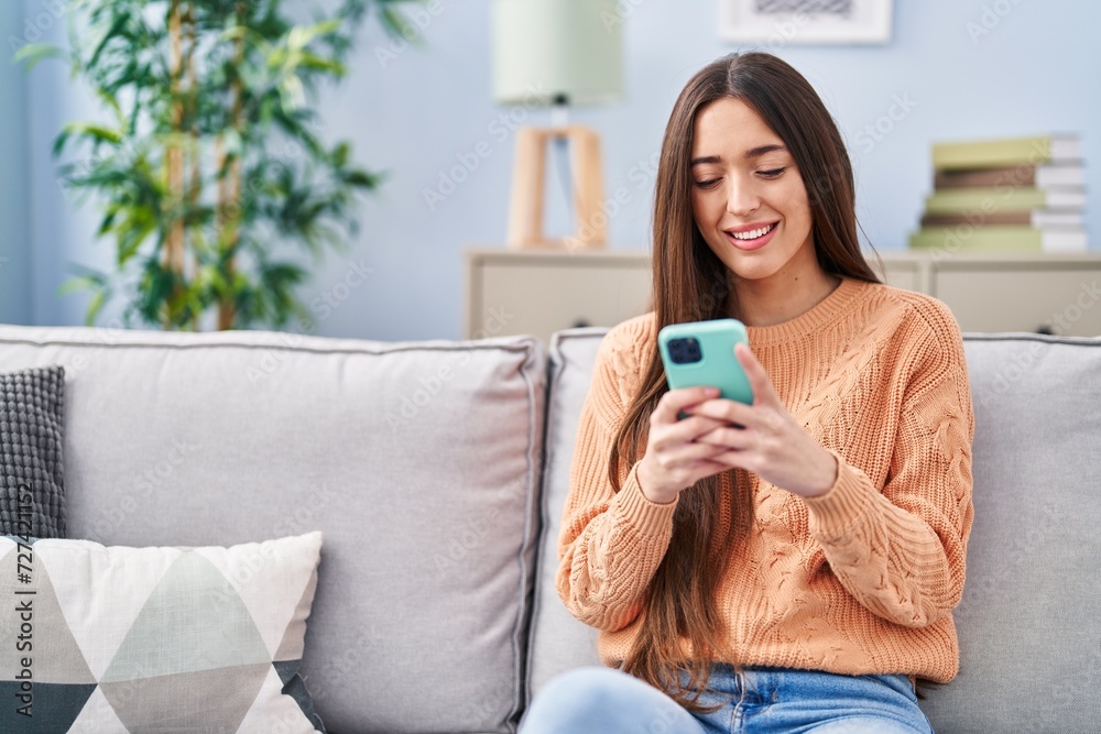 Young beautiful hispanic woman using smartphone sitting on sofa at home Young beautiful hispanic woman using smartphone sitting on sofa at home