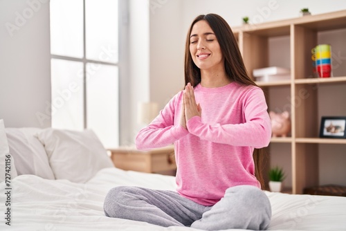 Young beautiful hispanic woman doing yoga exercise sitting on bed at bedroom