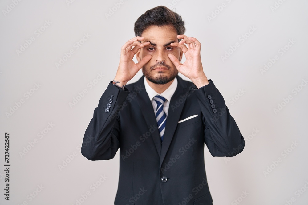 Young hispanic man with tattoos wearing business suit and tie trying to open eyes with fingers, sleepy and tired for morning fatigue Young hispanic man with tattoos wearing business suit and tie trying to open eyes with fingers, sleepy and tired for morning fatigue