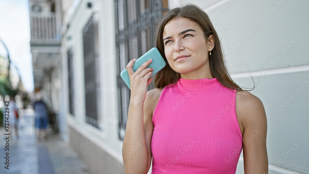 Relaxed, young and beautiful hispanic woman, with an attractive hairstyle, standing casually in a busy urban street, fully engrossed in an intense voice message on her smartphone Relaxed, young and beautiful hispanic woman, with an attractive hairstyle, standing casually in a busy urban street, fully engrossed in an intense voice message on her smartphone