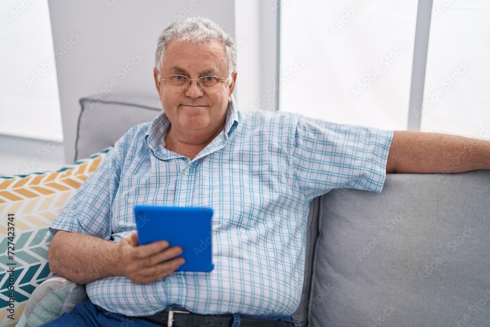 Middle age grey-haired man using touchpad sitting on sofa at home Middle age grey-haired man using touchpad sitting on sofa at home