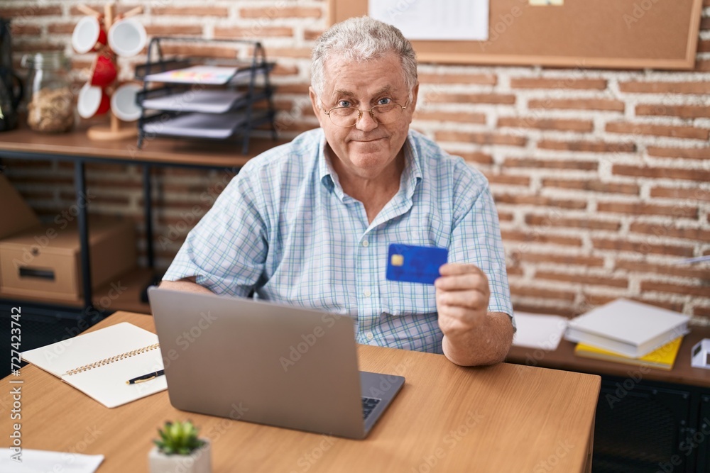Middle age grey-haired man business worker using laptop and credit card at office Middle age grey-haired man business worker using laptop and credit card at office