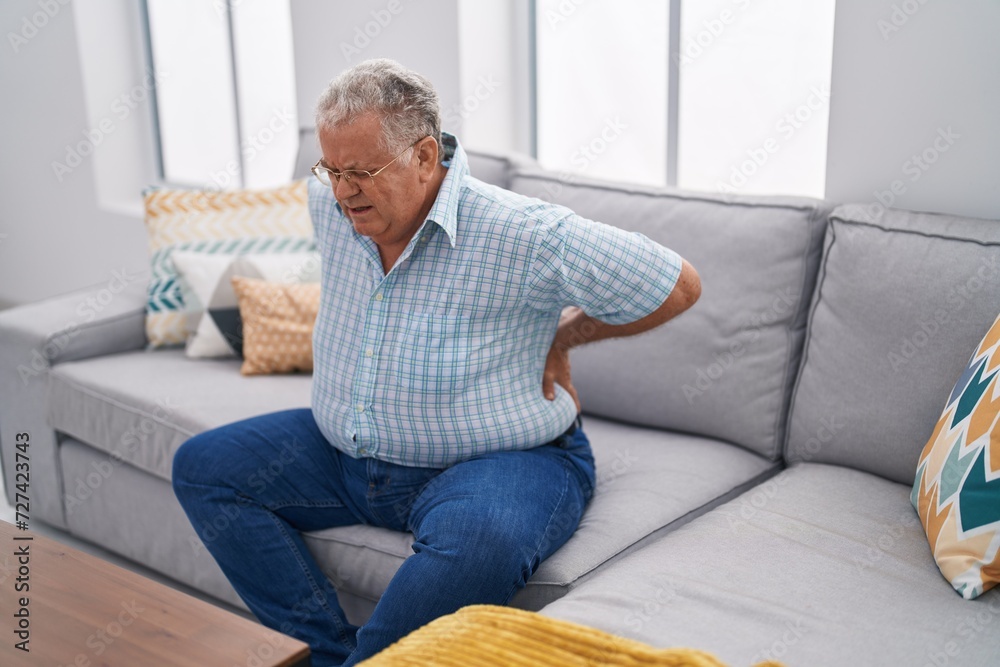 Middle age grey-haired man suffering for backache sitting on sofa at home