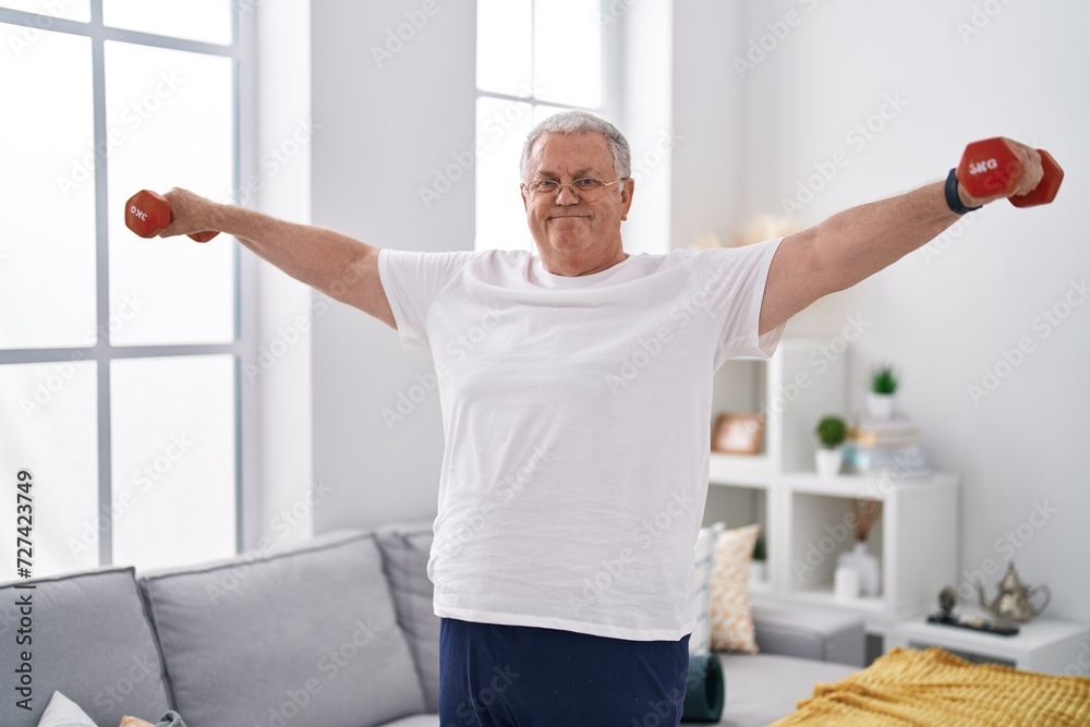 Obraz premium Middle age grey-haired man smiling confident using dumbbells training at home