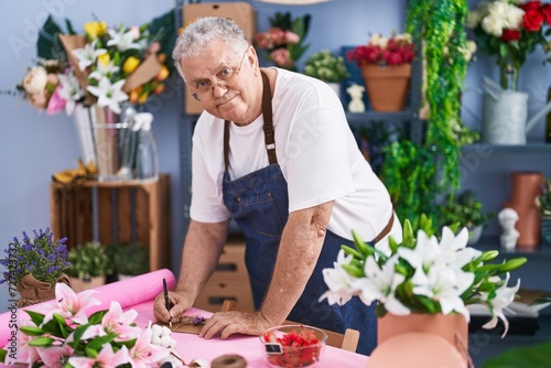 Middle age grey-haired man florist smiling confident writing on envelope letter at florist