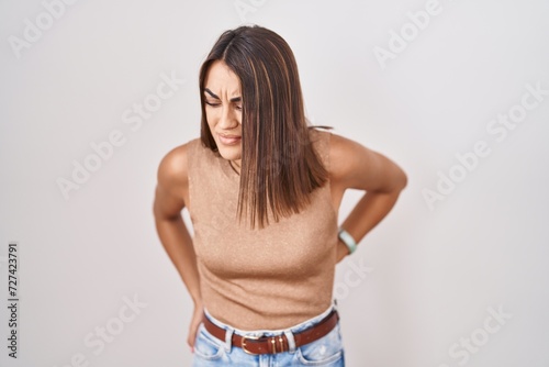 Young hispanic woman standing over white background suffering of backache, touching back with hand, muscular pain