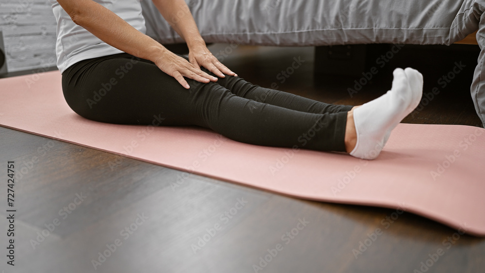 Obraz premium Morning bliss, awake and smiling caucasian woman in sportswear sitting on her bedroom floor, stretching legs while meditating for balance and relaxation at home