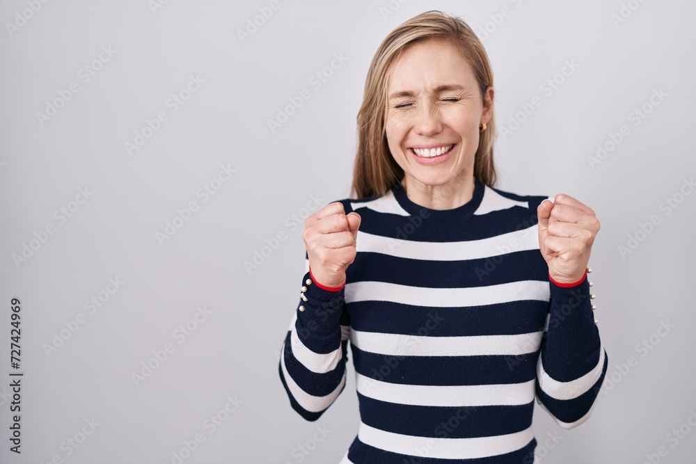 Young caucasian woman wearing casual navy sweater excited for success with arms raised and eyes closed celebrating victory smiling. winner concept. Young caucasian woman wearing casual navy sweater excited for success with arms raised and eyes closed celebrating victory smiling. winner concept.