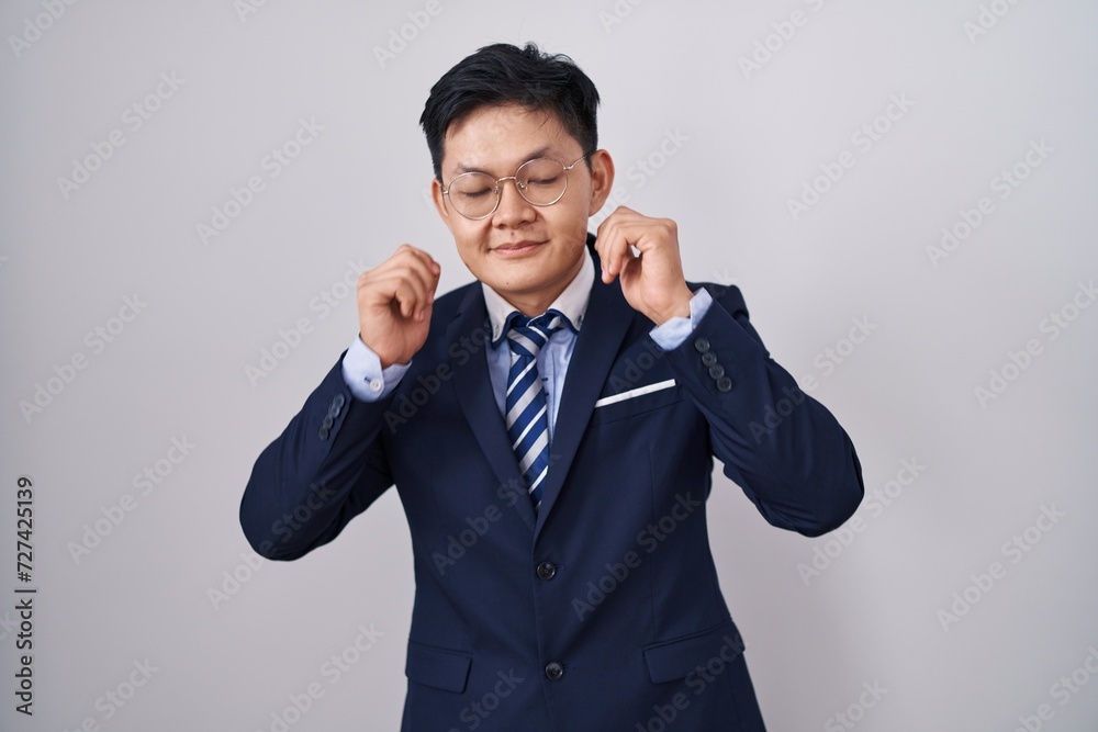 Young asian man wearing business suit and tie covering ears with fingers with annoyed expression for the noise of loud music. deaf concept. Young asian man wearing business suit and tie covering ears with fingers with annoyed expression for the noise of loud music. deaf concept.