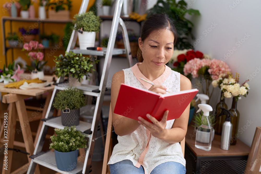 Young asian woman florist smiling confident writing on notebook at flower shop