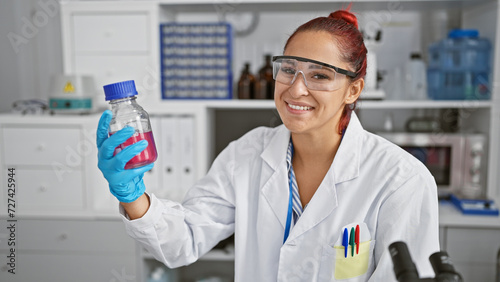 Inside the bustling lab, a confident young redhead scientist, beaming with a smile, expertly measures a elusive liquid in a bottle amidst the rhythmic humming of technology.