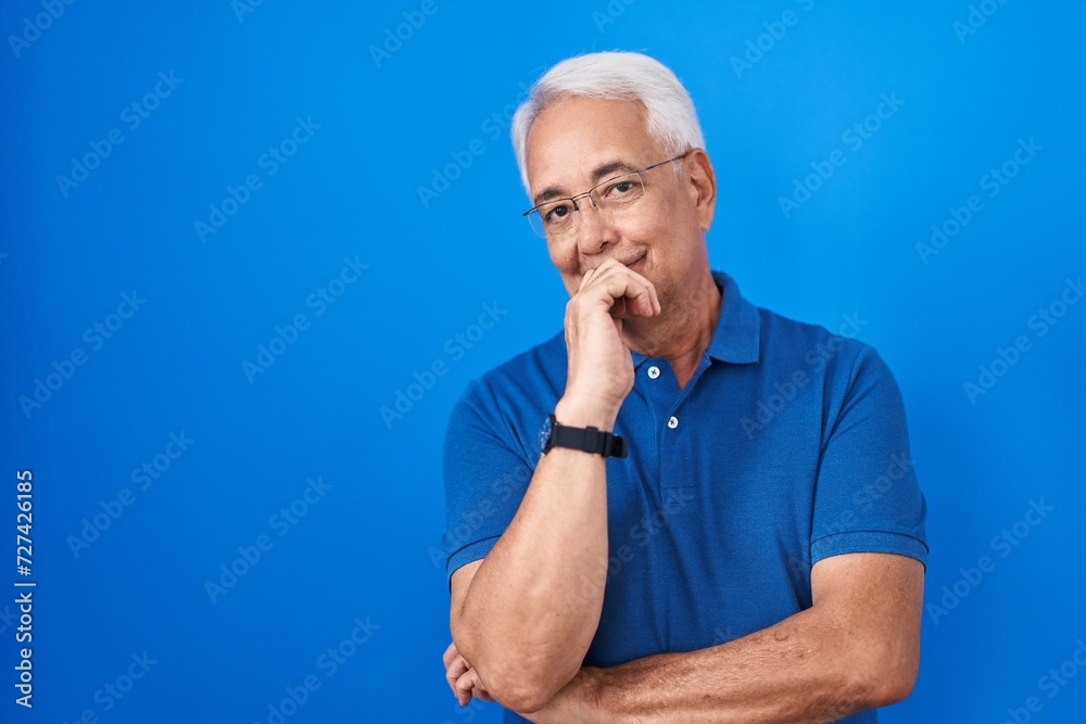 Middle age man with grey hair standing over blue background looking confident at the camera smiling with crossed arms and hand raised on chin. thinking positive. Middle age man with grey hair standing over blue background looking confident at the camera smiling with crossed arms and hand raised on chin. thinking positive.