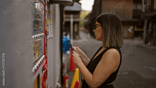 Beautiful hispanic woman with glasses uses phone to buy from kyoto's street vending machine, fusing traditional city charm and modern convenience photo