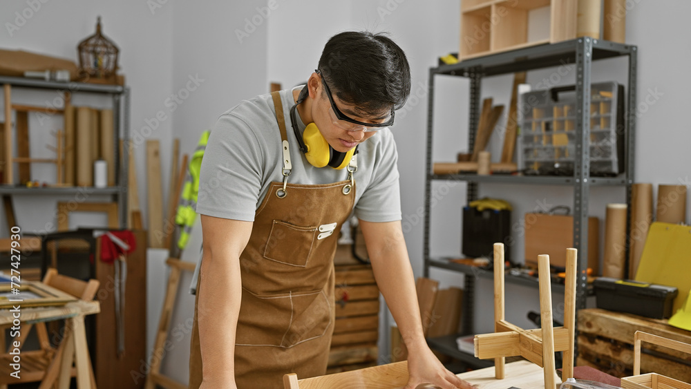 A young asian man examines wooden furniture intricately in a well-organized carpentry workshop. A young asian man examines wooden furniture intricately in a well-organized carpentry workshop.