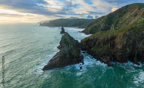 Aerial: Rocky coastline and ocean surf in the waitakere ranges at sunset. Whites Beach, Piha, Auckland, New Zealand. photo