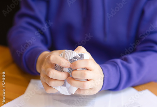 A crumpled and crumpled sheet of paper in the hands of a woman, paper ruined by hands. Female hands close-up with paper scribbled and crumpled, purple sweater, space for copy, text and advertising