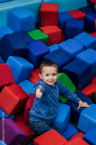 Little boy preschooler, happy smiling child lies playing with soft colored cubes in playroom, showing thumbs up, like. Photography, portrait, childhood concept.