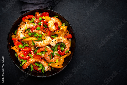 Hot stir fry shrimps with colorful paprika, green peas, chives and sesame seeds with ginger, garlic and soy sauce.   Black kitchen table background, top view