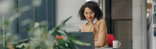 Stylish business woman in eyeglasses working on laptop while sitting in modern office near window