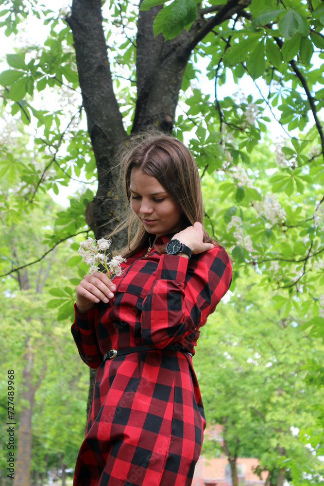 A young beautiful girl in a red plaid shirt and skirt in a park. A young beautiful girl in a red plaid shirt and skirt in a park.