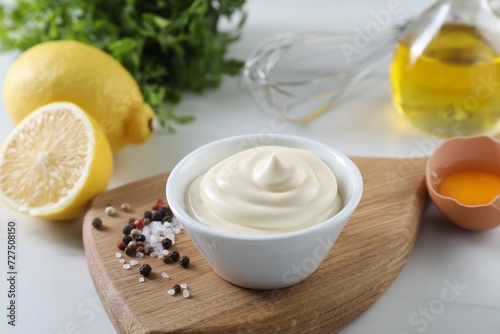 Tasty mayonnaise sauce in bowl, ingredients and spices on white table, closeup