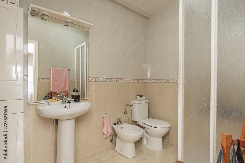 A bathroom with a white porcelain sink with a base of the same material under a frameless mirror with glass shelf and other matching toilets A bathroom with a white porcelain sink with a base of the same material under a frameless mirror with glass shelf and other matching toilets
