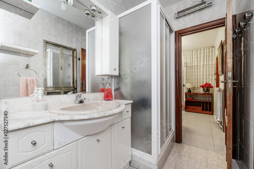 A small bathroom with white porcelain toilets on glossy white wooden furniture  framed mirror on the wall