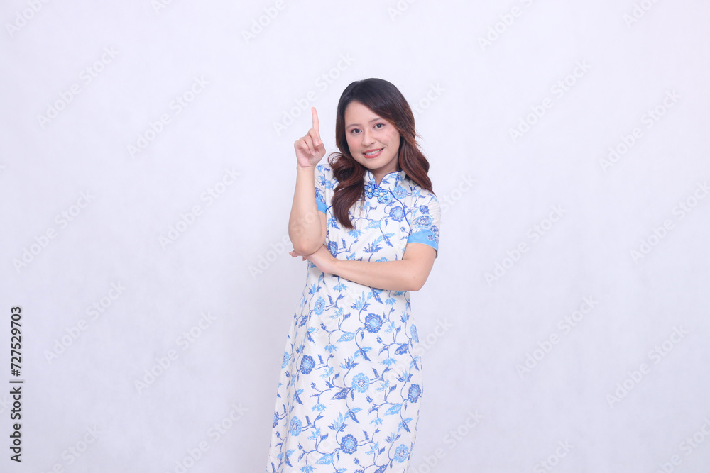 Beautiful smiling asian woman wearing modern chinese dress arms crossed pointing up isolated on white background. happy Chinese New Year Beautiful smiling asian woman wearing modern chinese dress arms crossed pointing up isolated on white background. happy Chinese New Year
