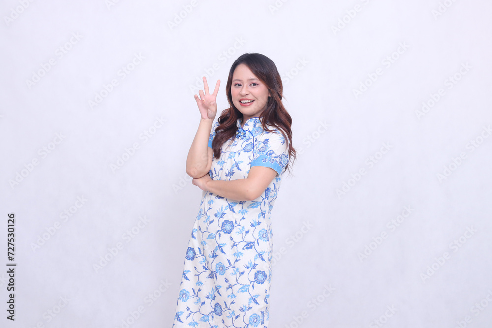 Beautiful asian woman smiling crookedly wearing modern chinese dress right hand marked 2 dua or peace isolated on white background. happy Chinese New Year Beautiful asian woman smiling crookedly wearing modern chinese dress right hand marked 2 dua or peace isolated on white background. happy Chinese New Year