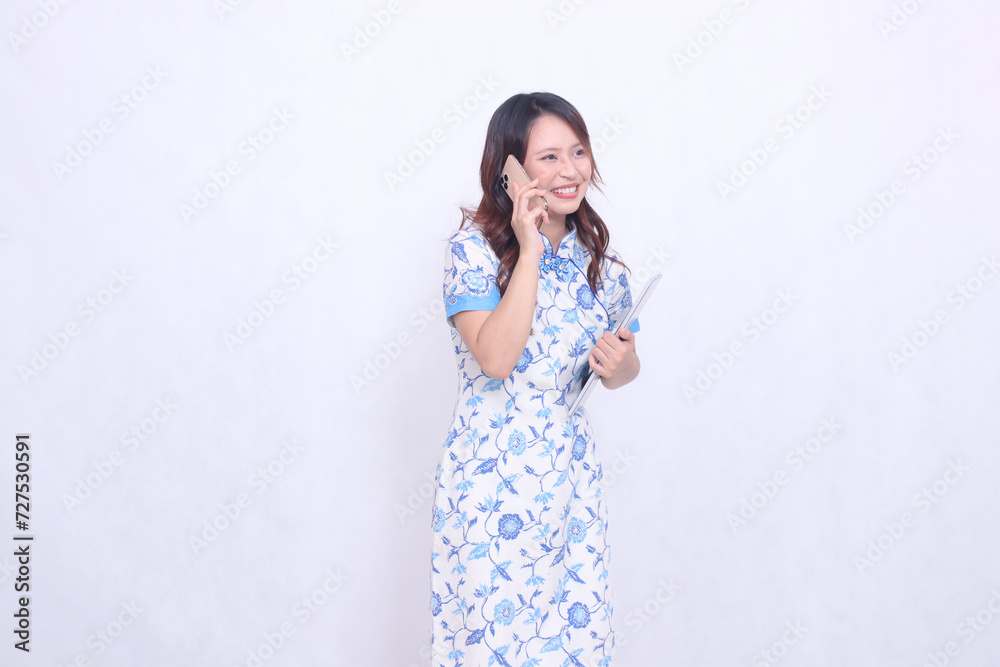 beautiful cheerful Indonesian Chinese woman looking sideways top left wearing modern Chinese blue dress holding tablet holding phone isolated white background beautiful cheerful Indonesian Chinese woman looking sideways top left wearing modern Chinese blue dress holding tablet holding phone isolated white background