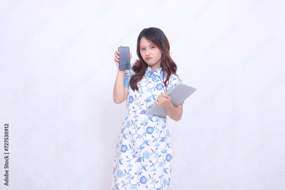 beautiful asian woman wearing blue chinese dress upset holding tablet and looking at cell phone screen isolated white background beautiful asian woman wearing blue chinese dress upset holding tablet and looking at cell phone screen isolated white background