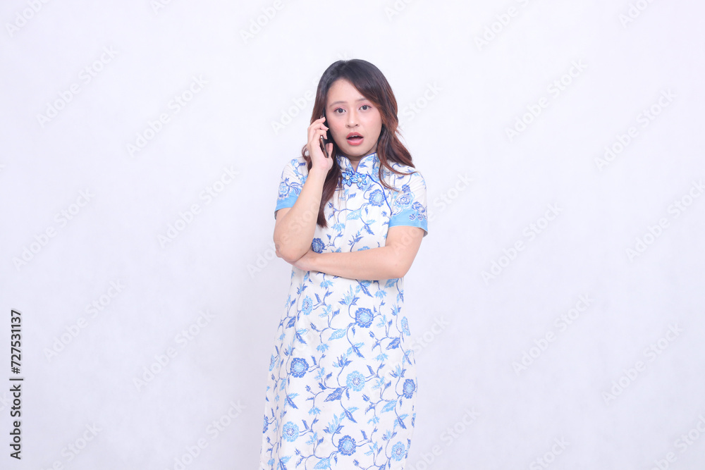 young asian javanese chinese woman very shocked wearing blue chinese dress while on the phone looking at the camera isolated white background young asian javanese chinese woman very shocked wearing blue chinese dress while on the phone looking at the camera isolated white background