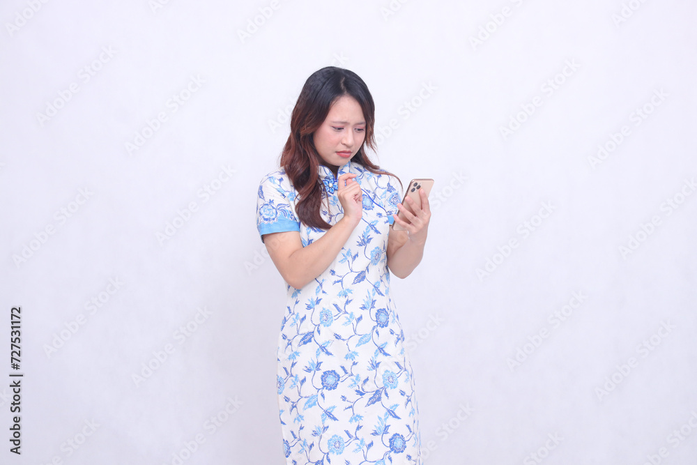 Disappointed Young Asian Javanese Chinese Woman Wearing Left Slanted Chinese Blue Dress While Operating Gadget Forefinger Pressing Mobile Phone Isolated White Background Disappointed Young Asian Javanese Chinese Woman Wearing Left Slanted Chinese Blue Dress While Operating Gadget Forefinger Pressing Mobile Phone Isolated White Background