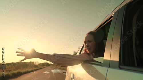Smiling travel woman road trip riding car with hand in window at sunset sunrise enjoy freedom air closeup slowmo. Happy young tourist female at movement automobile with summer nature rural scenery