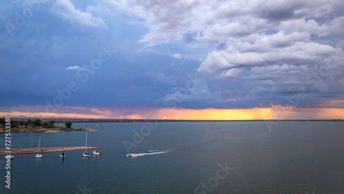  We see a beautiful sunset, sailboats parked in the waters of the lake, in the background a cloudy sky full of colors and textures, a great storm and rain approaching, El Carrizal dam, Mendoza Arg.