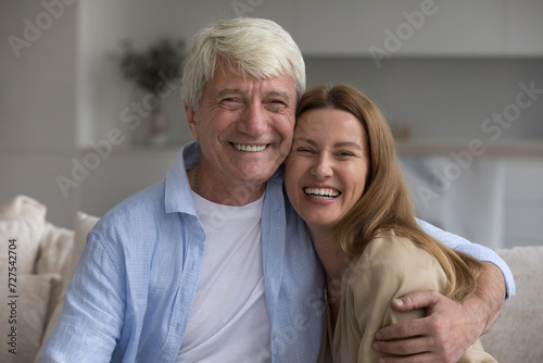 Happy grey haired senior daddy embracing beautiful adult daughter child, looking at camera, smiling, laughing, enjoying leisure, close relationship, affection. Family head shot portrait