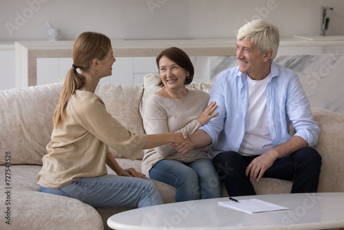 Positive senior couple shaking hand of real estate agent, financial consultant at home, smiling, thanking for consultation. Older customer and expert shaking hands over contract, agreement