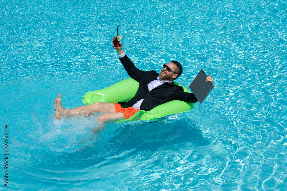 Freelance work, distance online work, e-working. Summer business. Business man in suit drink summer cocktail and using laptop in pool. Businessman dreams on summer business in swimming pool water.