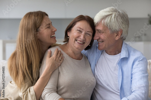 Happy excited senior lady enjoying leisure with family, looking at camera, celebrating mothers day. Adult daughter woman and older husband hugging cheerful mature mom with love, joy. Family portrait