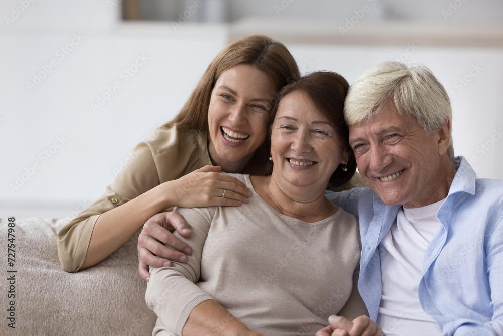 Happy senior woman enjoying warm good relationship with adult daughter and loving older husband, posing with family for shooting, looking away, smiling, laughing Happy senior woman enjoying warm good relationship with adult daughter and loving older husband, posing with family for shooting, looking away, smiling, laughing