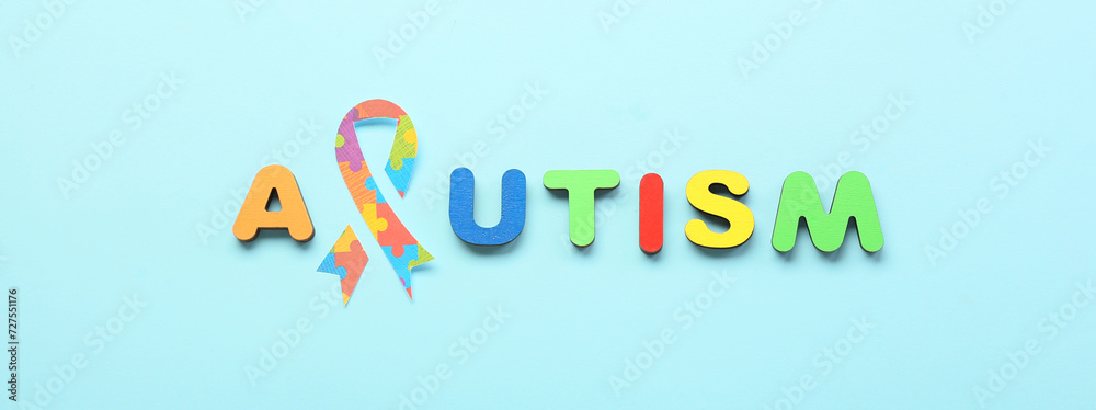 Word AUTISM with paper awareness ribbon on light blue background Word AUTISM with paper awareness ribbon on light blue background